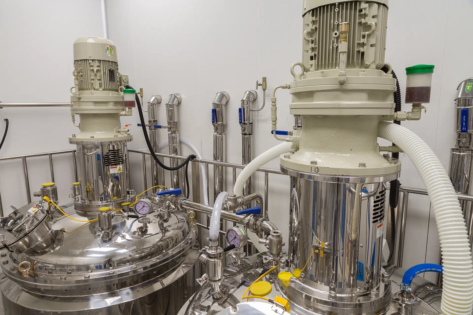Two stainless steel mixing vessels with top-mounted agitator motors, pressure gauges and hoses in a lab