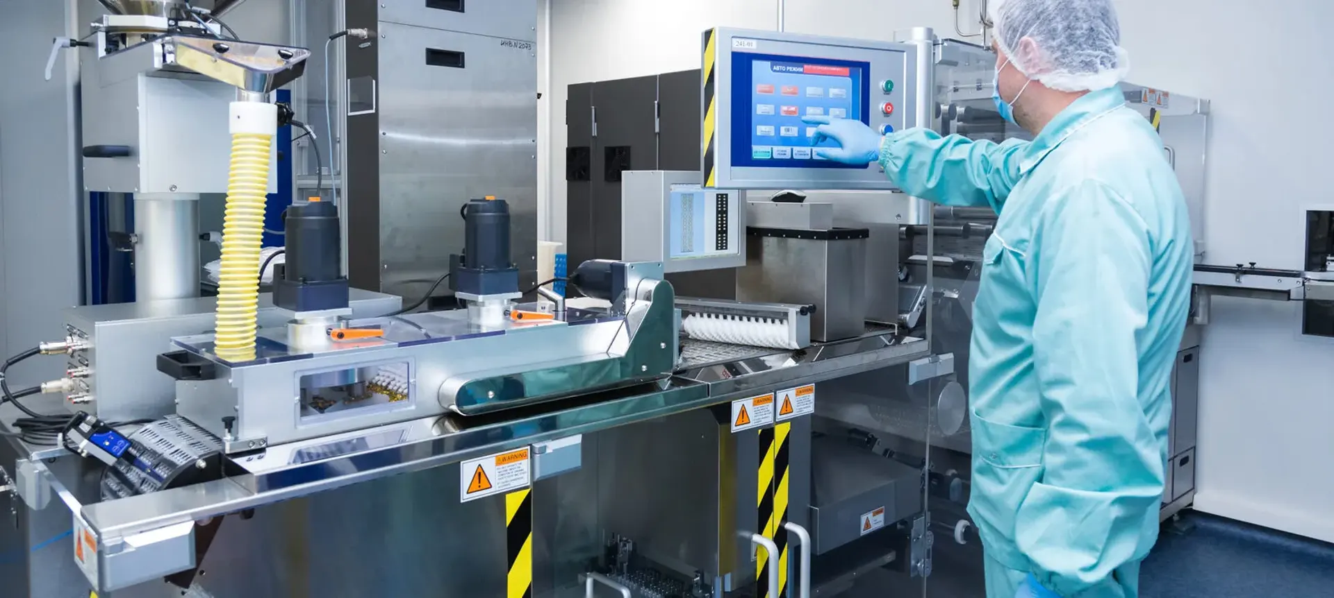 Operator in protective clothing using the touchscreen on an industrial packaging machine in a clean production room