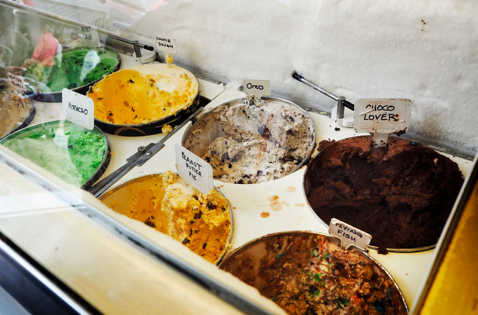 Tubs of ice cream in a display freezer with handwritten flavour labels such as pistachio and cookie dough
