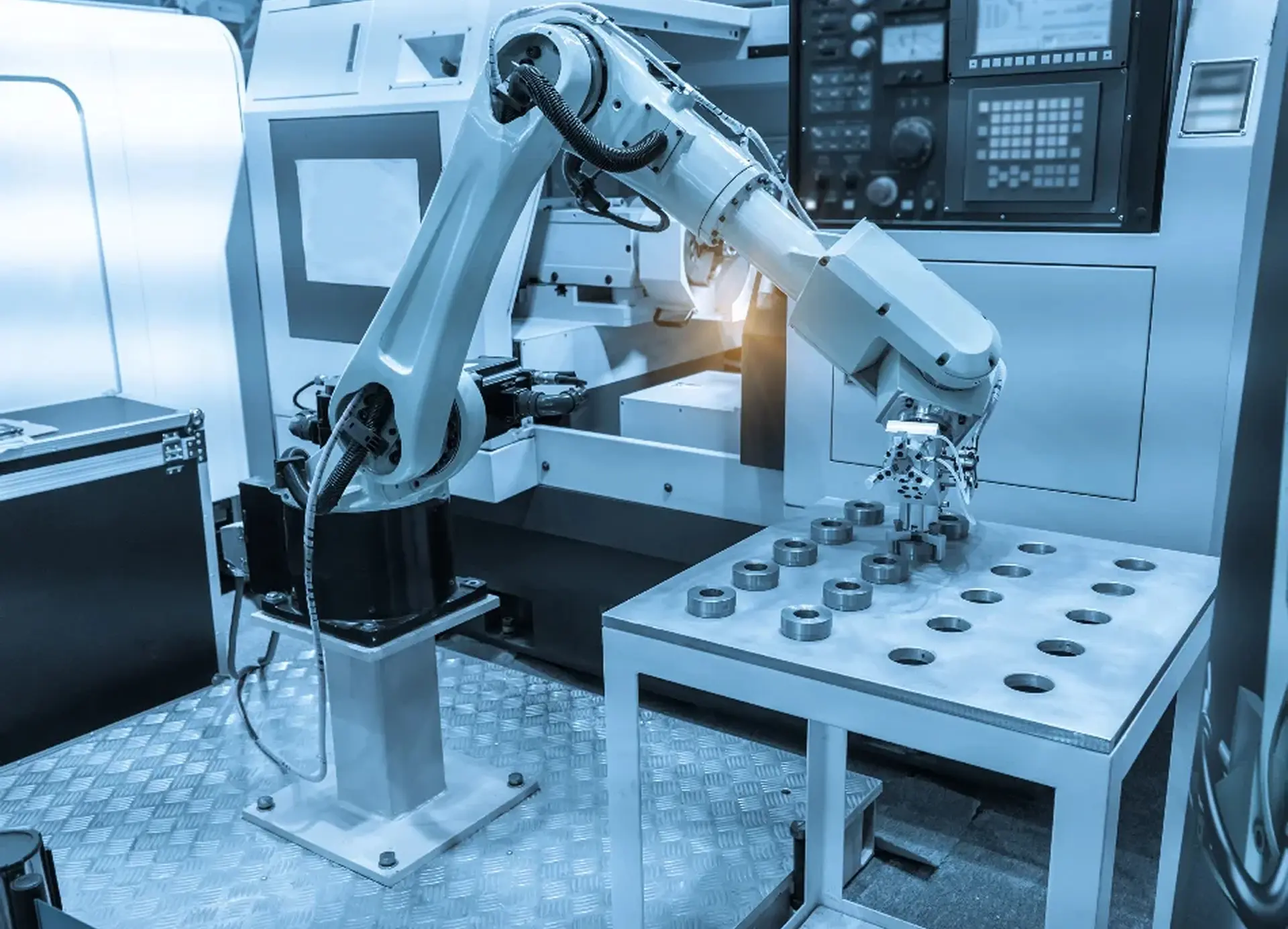 White robotic arm placing metal parts on a steel table beside a CNC machine in an automated factory cell