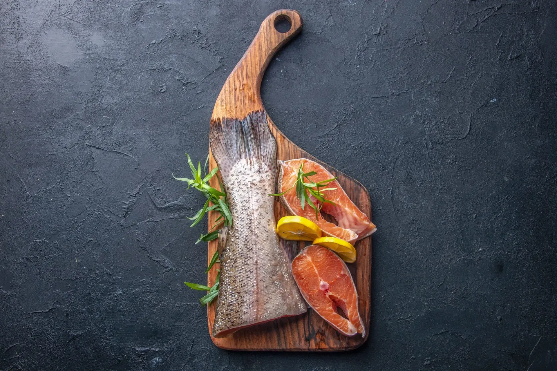 Top view of sliced fresh fish with lemon on a dark surface
