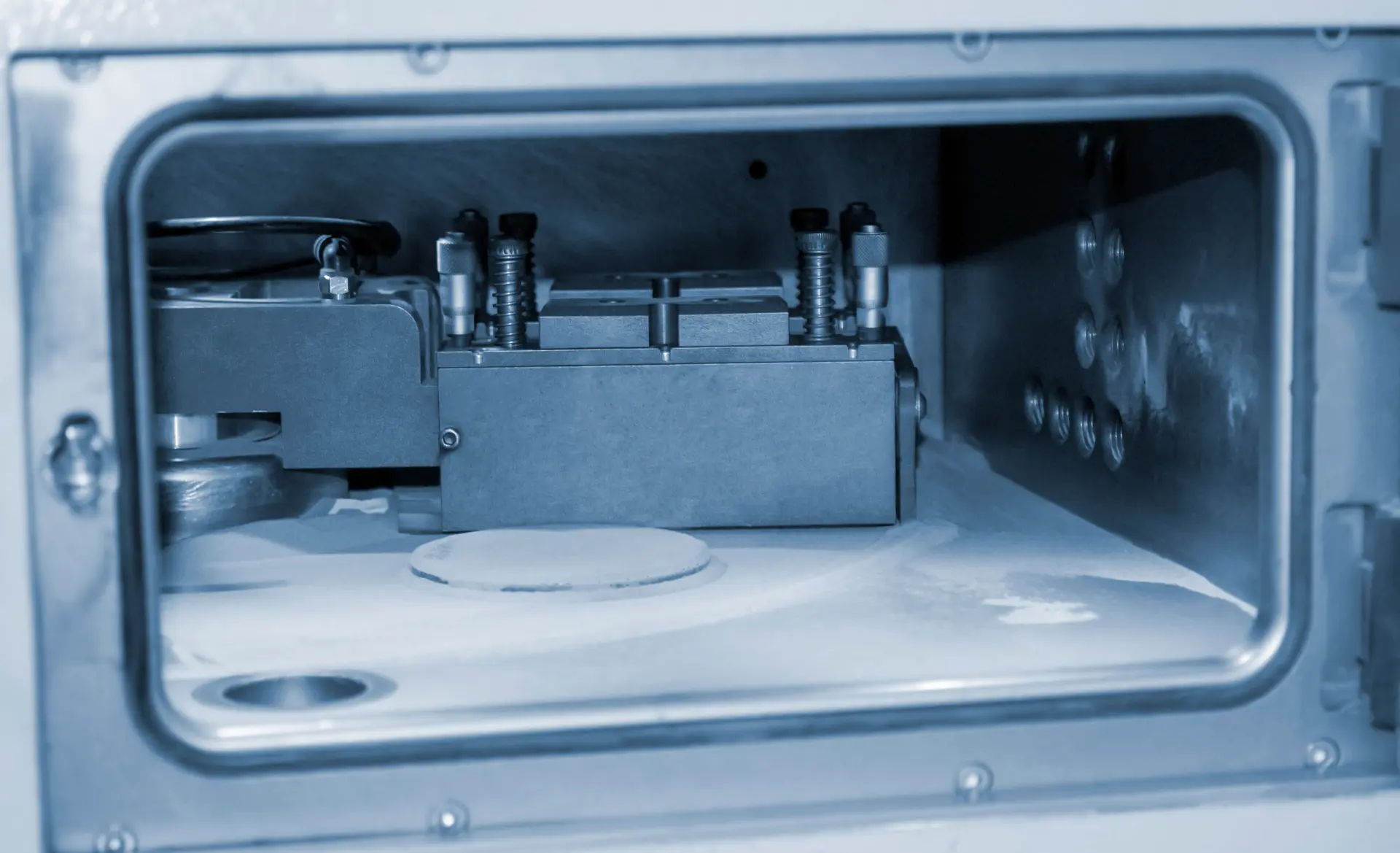 Inside view of a stainless steel vacuum chamber with a clamped sample holder above a round sample disc