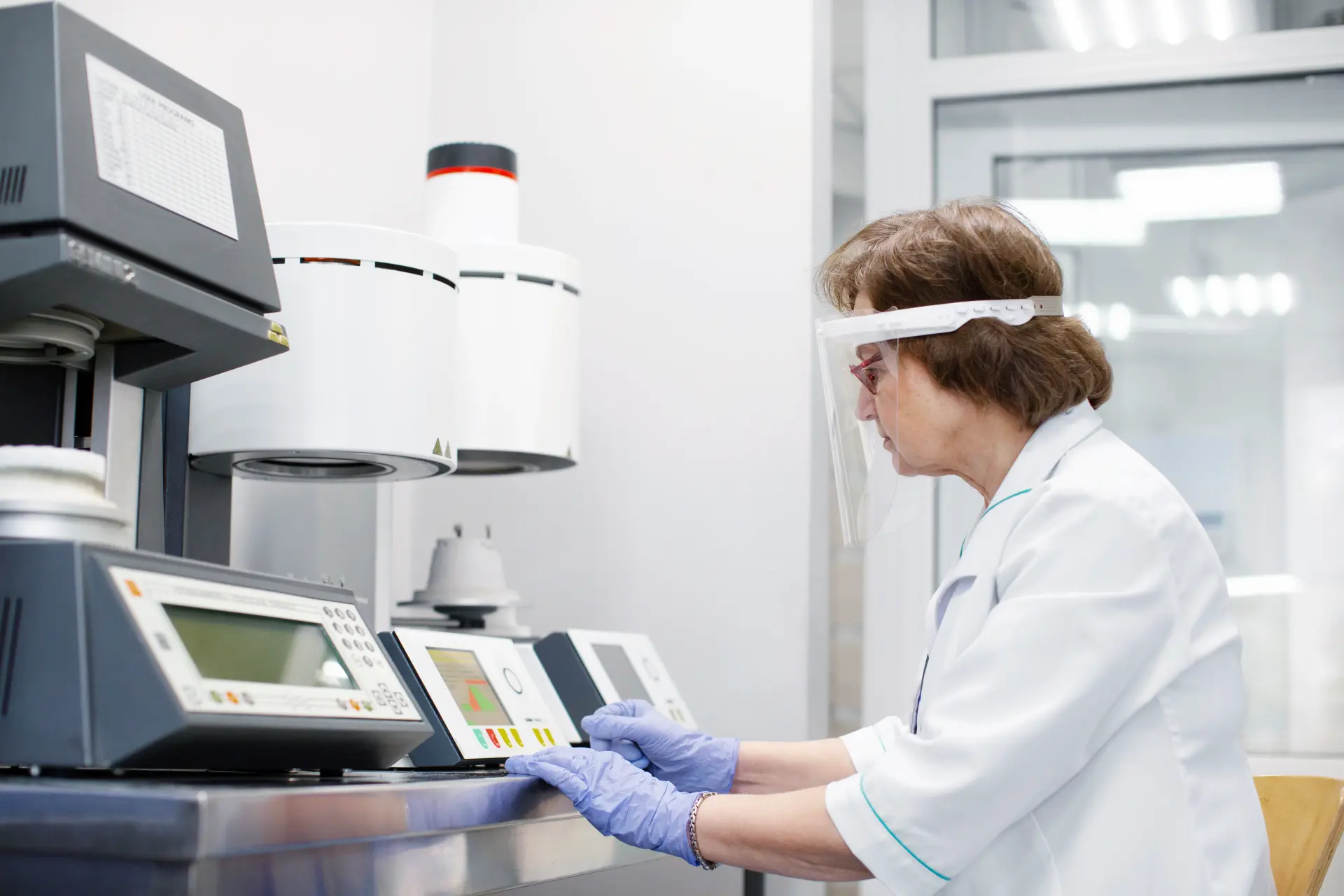 Lab technician in a face shield and gloves using benchtop analytical instruments with digital displays