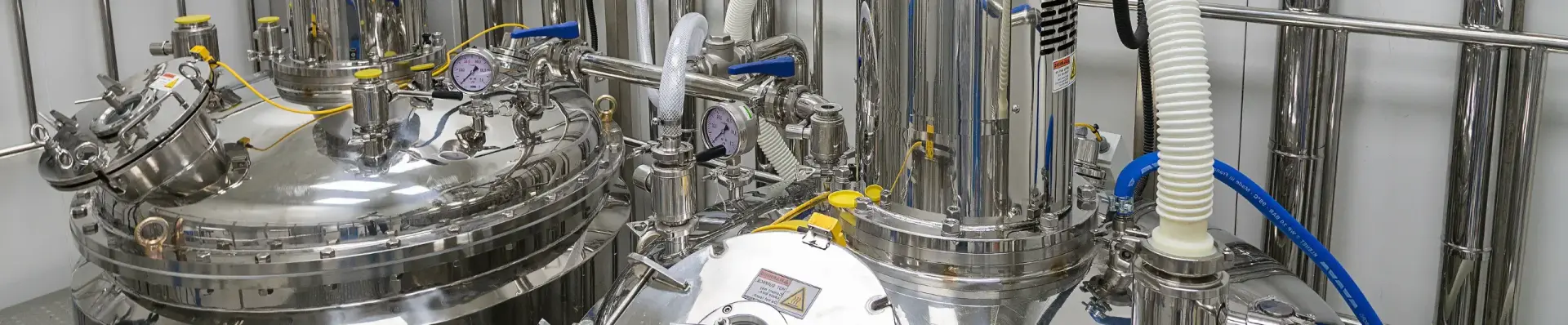 Stainless steel process vessels fitted with pressure gauges, valves and hoses in a production facility