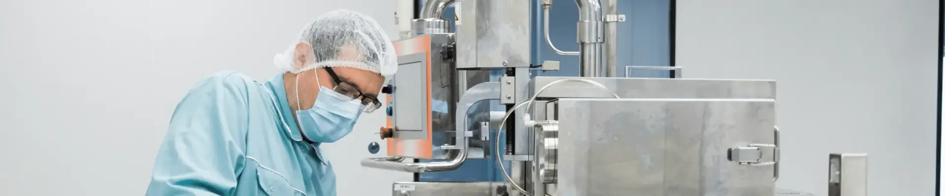 Worker in a hairnet, face mask and glasses operating stainless steel processing equipment in a cleanroom