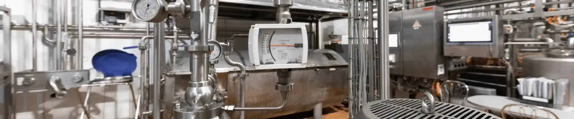 Stainless steel pipework, pressure gauges and a flow meter inside a food processing plant